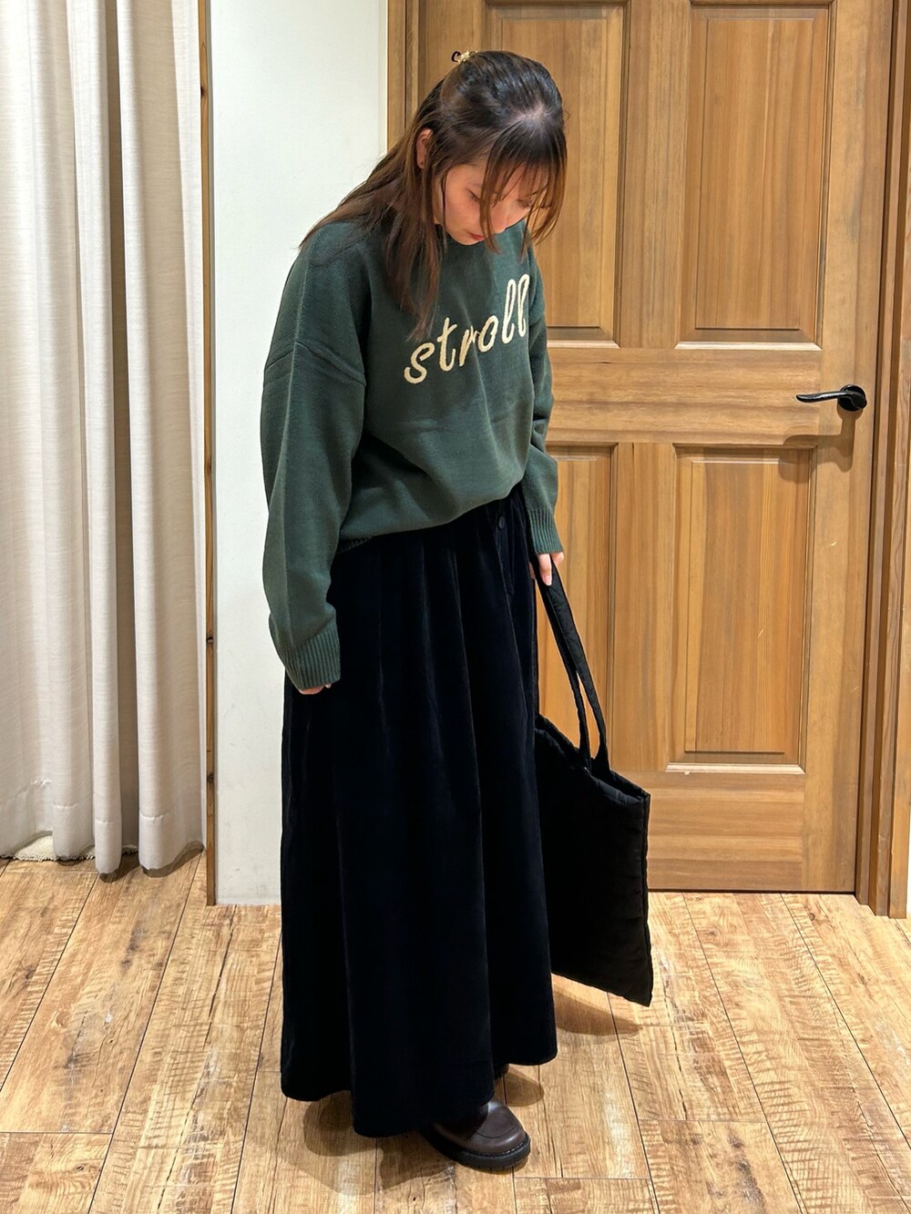 グリーン系のニット/セーター、ブラック系のスカート、ベージュ系のハンドバッグを着用したレディースの秋コーディネートの4枚目の写真