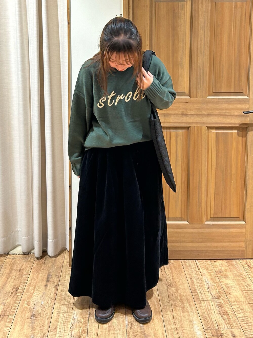 グリーン系のニット/セーター、ブラック系のスカート、ベージュ系のハンドバッグを着用したレディースの秋コーディネートの2枚目の写真