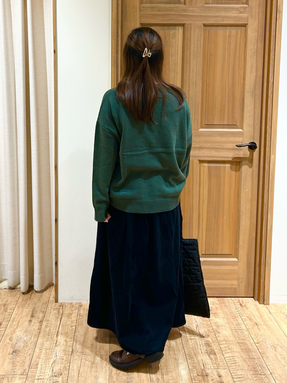 グリーン系のニット/セーター、ブラック系のスカート、ベージュ系のハンドバッグを着用したレディースの秋コーディネートの5枚目の写真