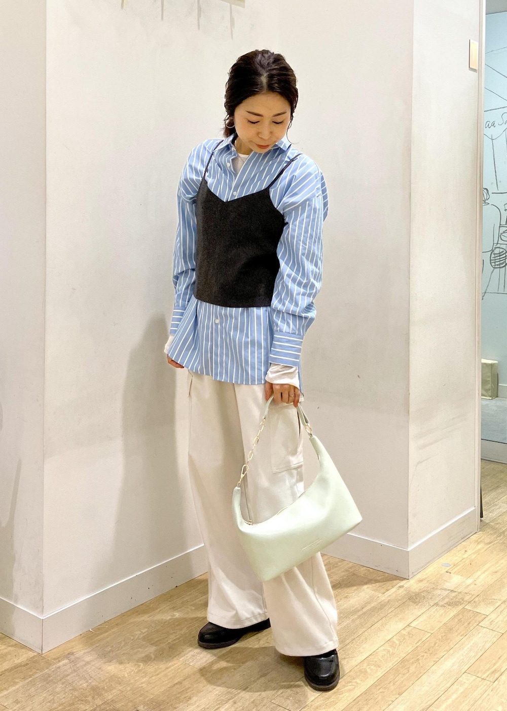 グレー系のニット/セーター、グリーン系のショルダーバッグ、ブルー系のシャツ/ブラウスを着用したレディースの春コーディネートの2枚目の写真