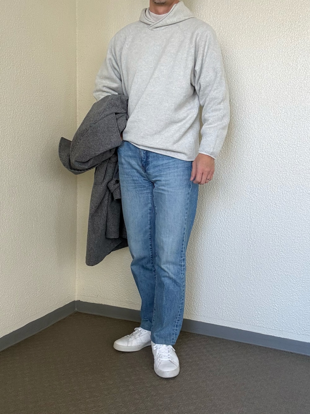グレー系のステンカラーコート、ブルー系のデニムパンツ、ホワイト系のスニーカーを着用したメンズの冬コーディネートの2枚目の写真