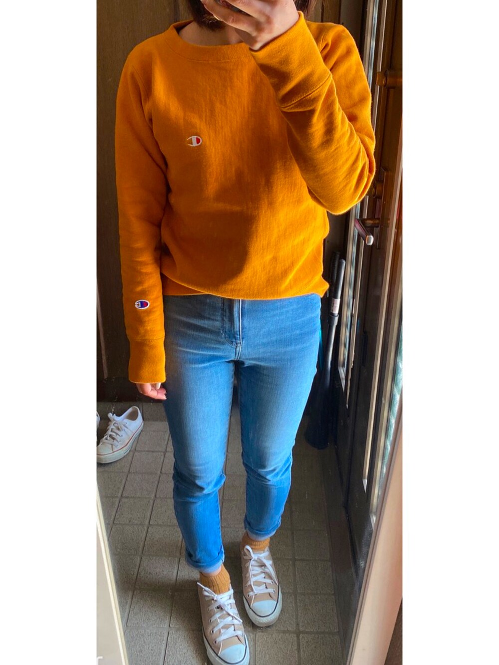 オレンジ系のスウェット、ブルー系のデニムパンツ、ベージュ系のスニーカーを着用したレディースの春コーディネートの2枚目の写真