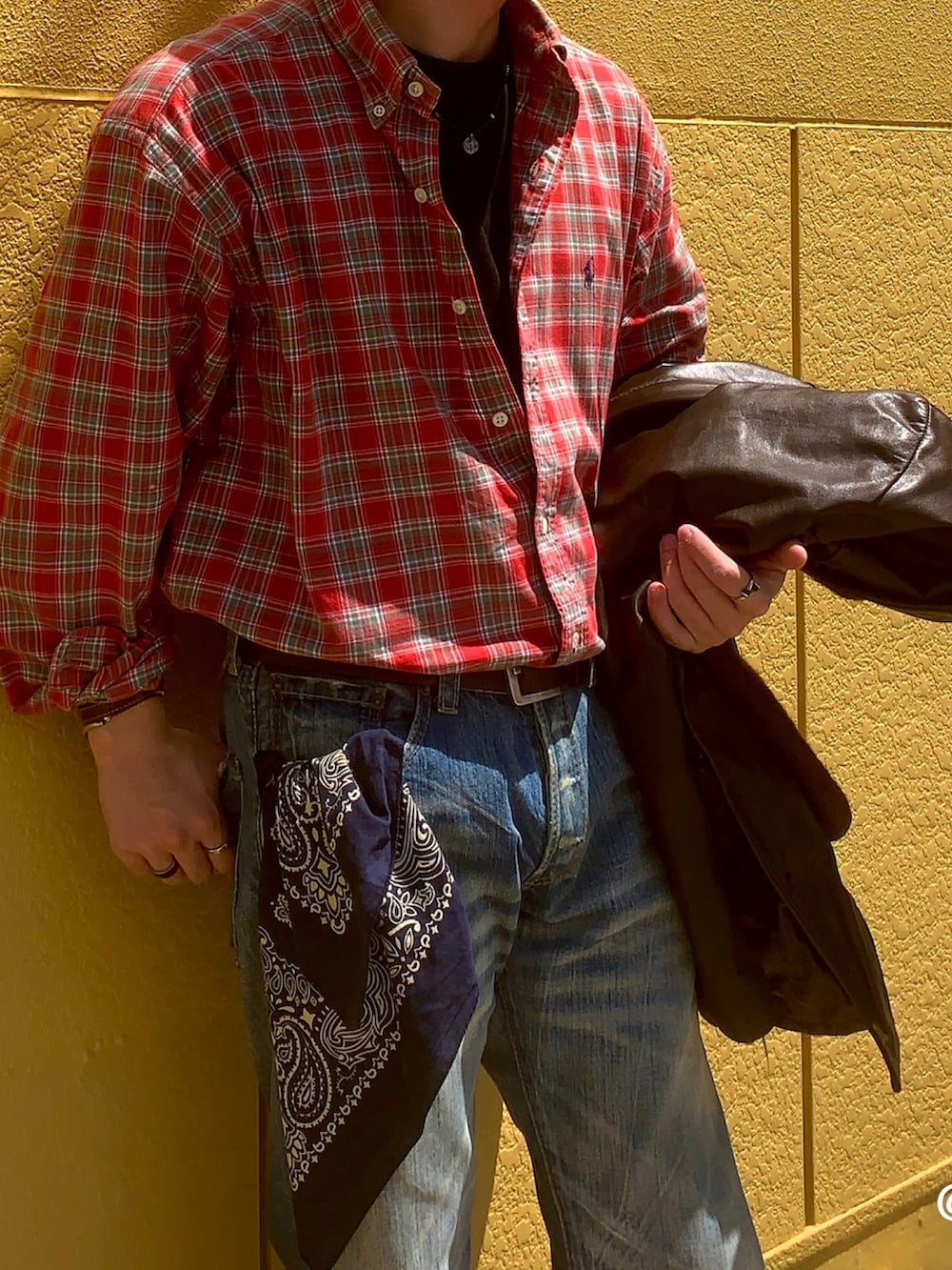 ブラック系のドレスシューズ、レッド系のトップス、ブルー系のデニムパンツを着用したメンズの春コーディネートの3枚目の写真