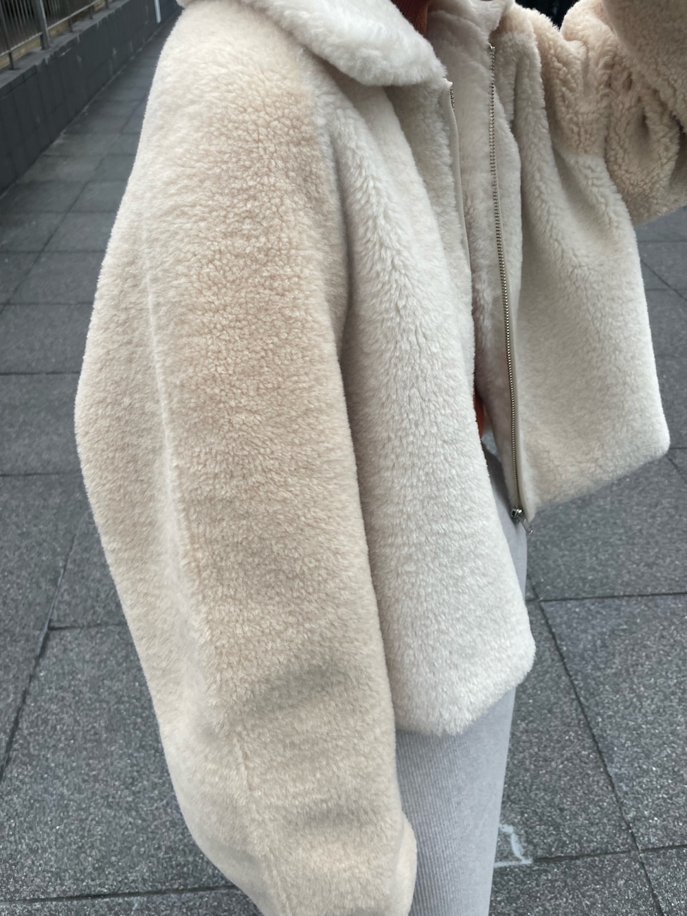 ホワイト系のブルゾン、オレンジ系のニット/セーター、グレー系のスカートを着用したレディースの冬コーディネートの5枚目の写真