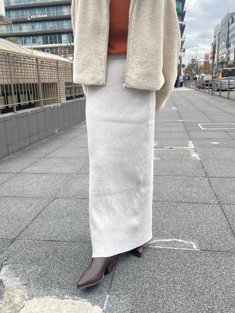 ホワイト系のブルゾン、オレンジ系のニット/セーター、グレー系のスカートを着用したレディースの冬コーディネートの6枚目の写真