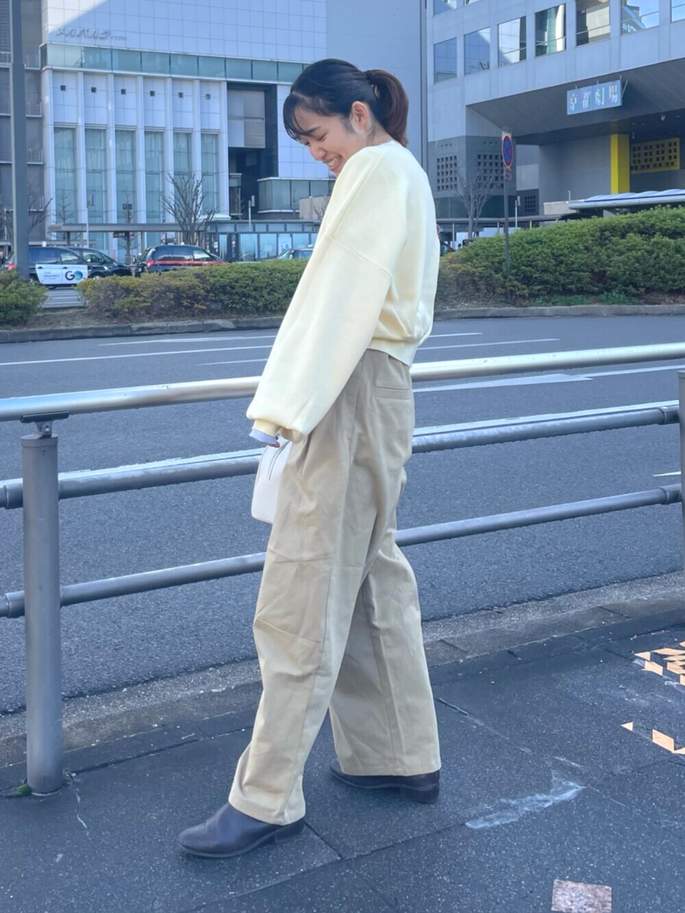 イエロー系のニット/セーター、ベージュ系のチノパンツ、ホワイト系のボストンバッグを着用したレディースの冬コーディネートの2枚目の写真