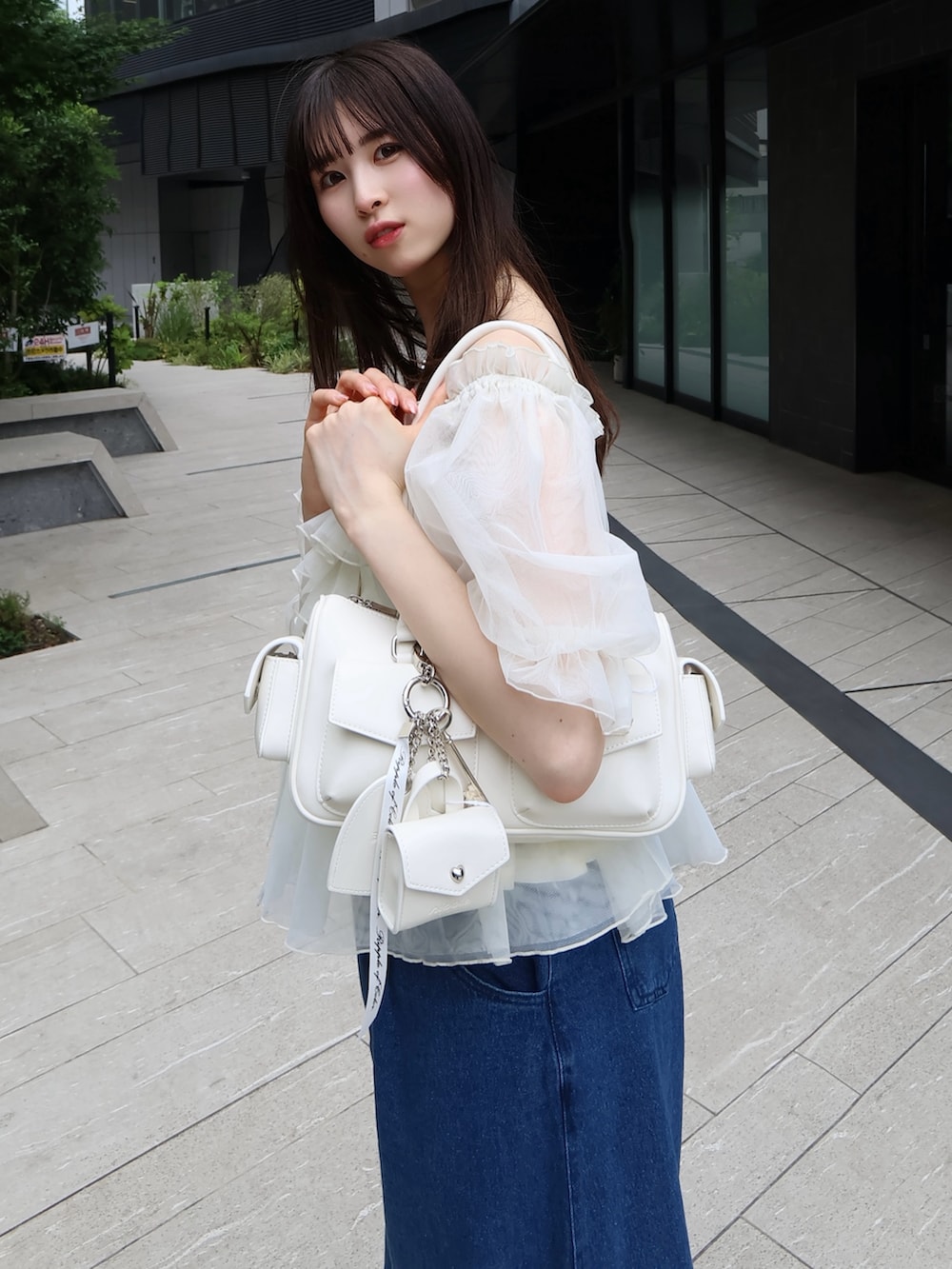 ホワイト系のボストンバッグ、ホワイト系のシャツ/ブラウス、ブルー系のデニムパンツを着用したレディースの夏コーディネートの3枚目の写真