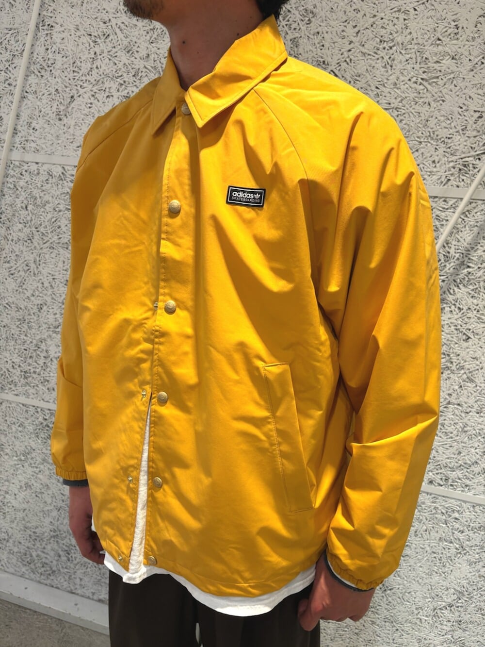 イエロー系のブルゾン、ブラック系のスニーカー、ブラック系のアクセサリーを着用したメンズの冬コーディネートの3枚目の写真