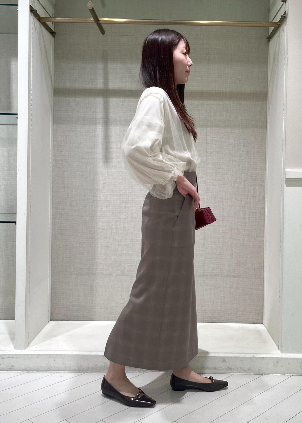 レッド系のショルダーバッグ、ブラウン系のパンプス、ベージュ系のスカートを着用したレディースの秋コーディネートの2枚目の写真