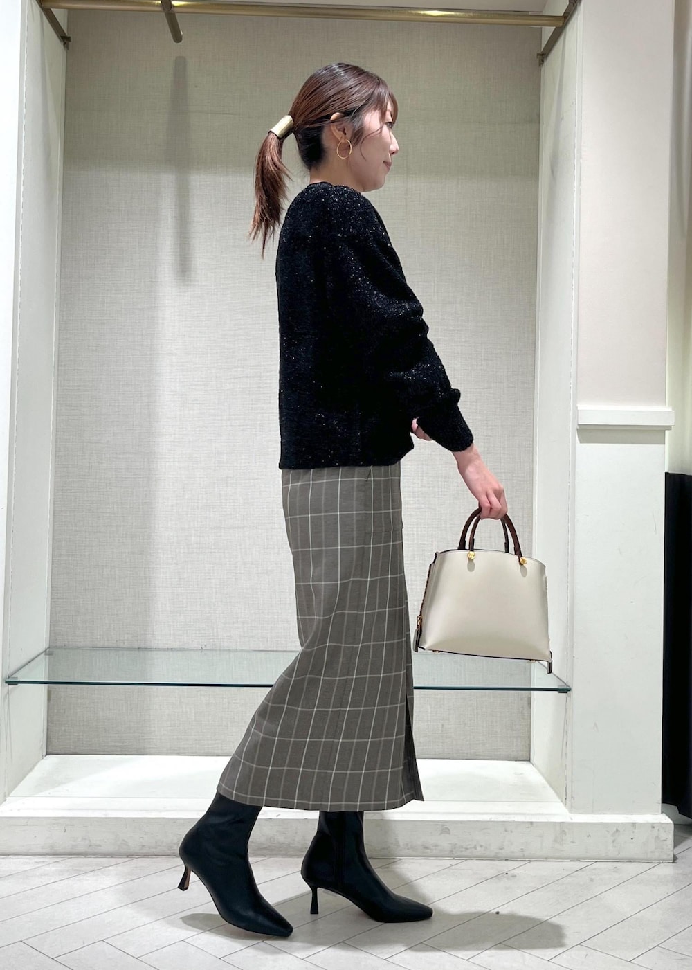 ホワイト系のハンドバッグ、ブラック系のブーツ、ブラウン系のスカートを着用したレディースの秋コーディネートの2枚目の写真