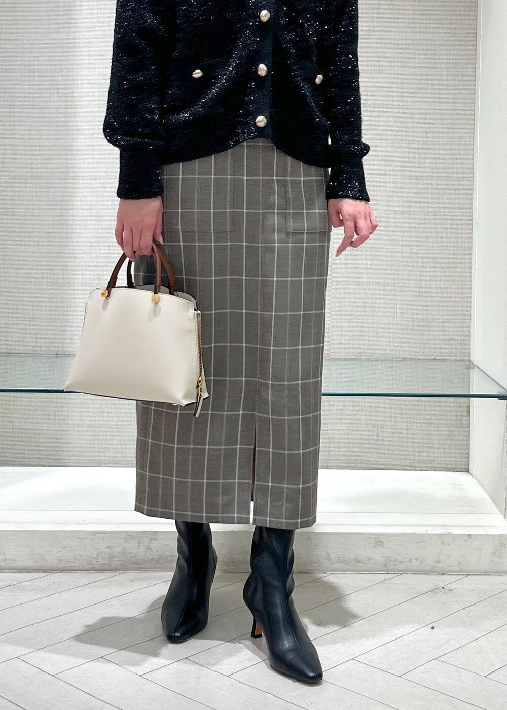 ホワイト系のハンドバッグ、ブラック系のブーツ、ブラウン系のスカートを着用したレディースの秋コーディネートの6枚目の写真