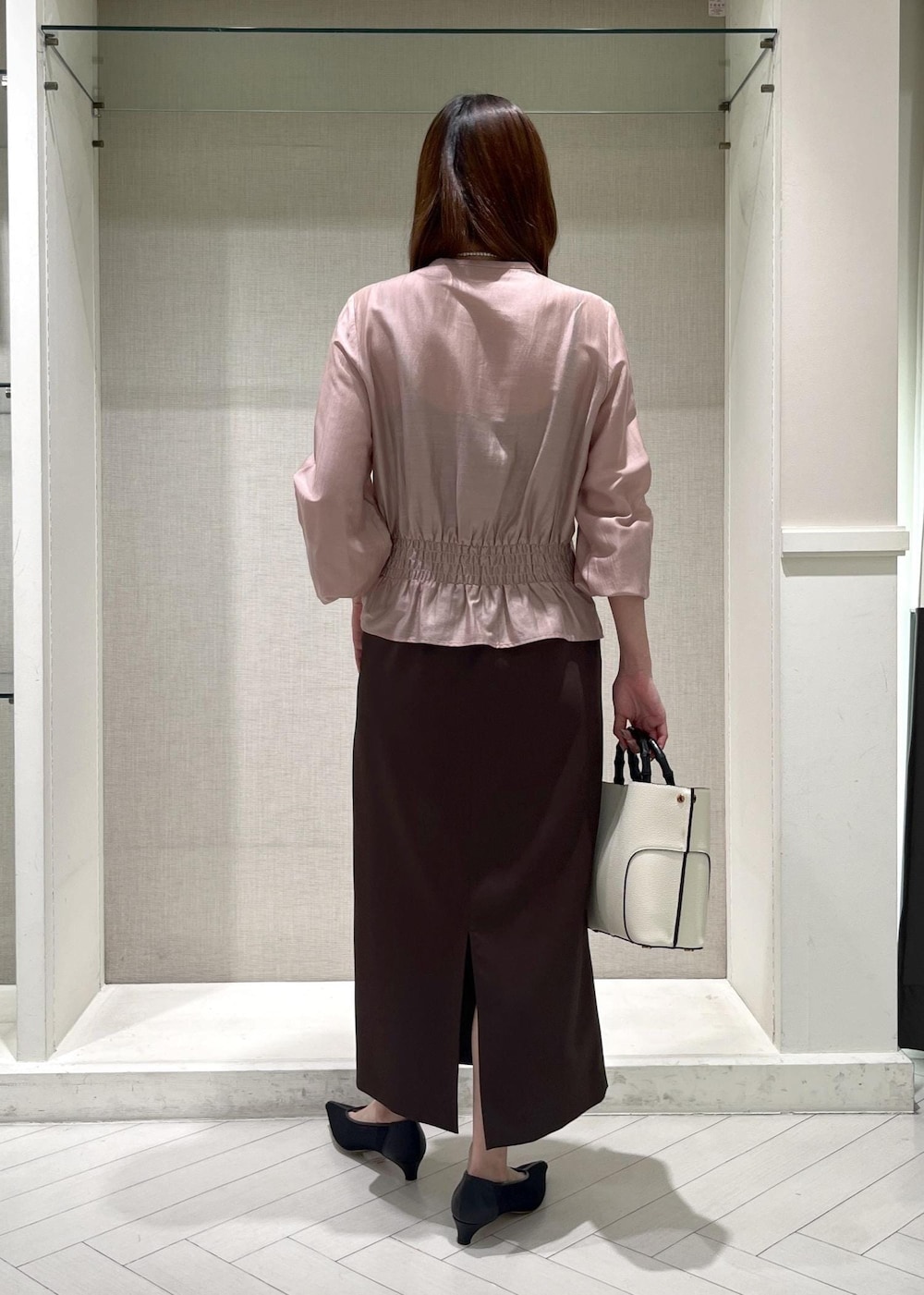 ブラック系のパンプス、ホワイト系のハンドバッグ、ブラウン系のスカートを着用したレディースの春コーディネートの3枚目の写真