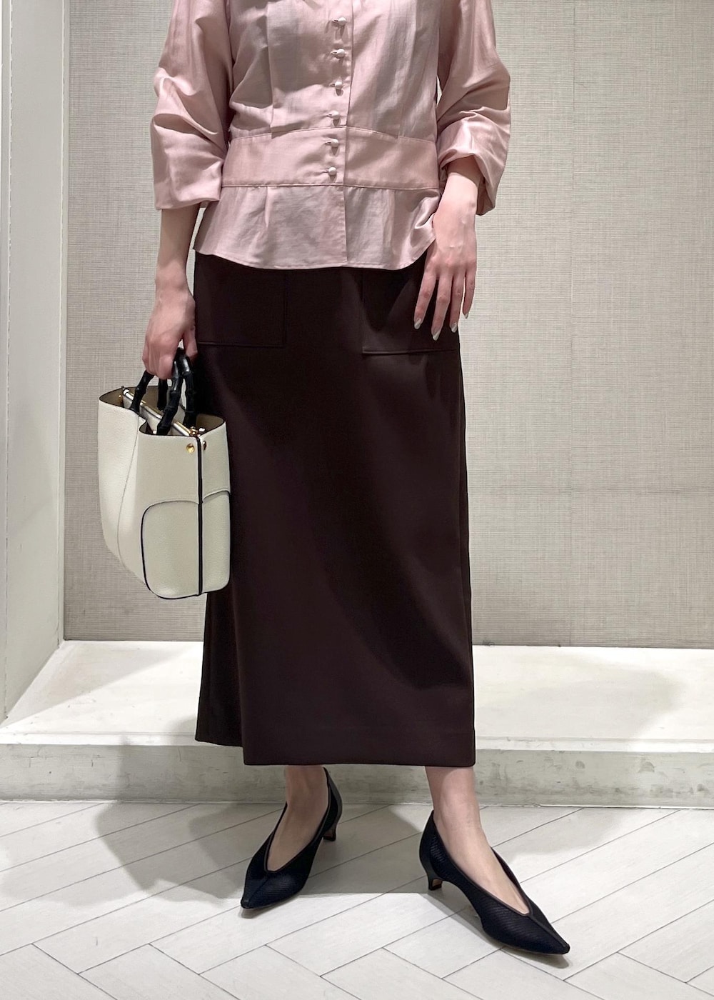 ブラック系のパンプス、ホワイト系のハンドバッグ、ブラウン系のスカートを着用したレディースの春コーディネートの6枚目の写真