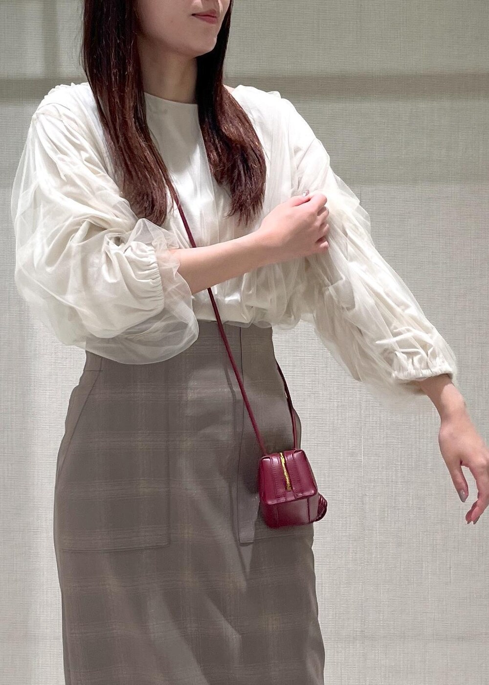 レッド系のショルダーバッグ、ブラウン系のパンプス、ベージュ系のスカートを着用したレディースの秋コーディネートの4枚目の写真