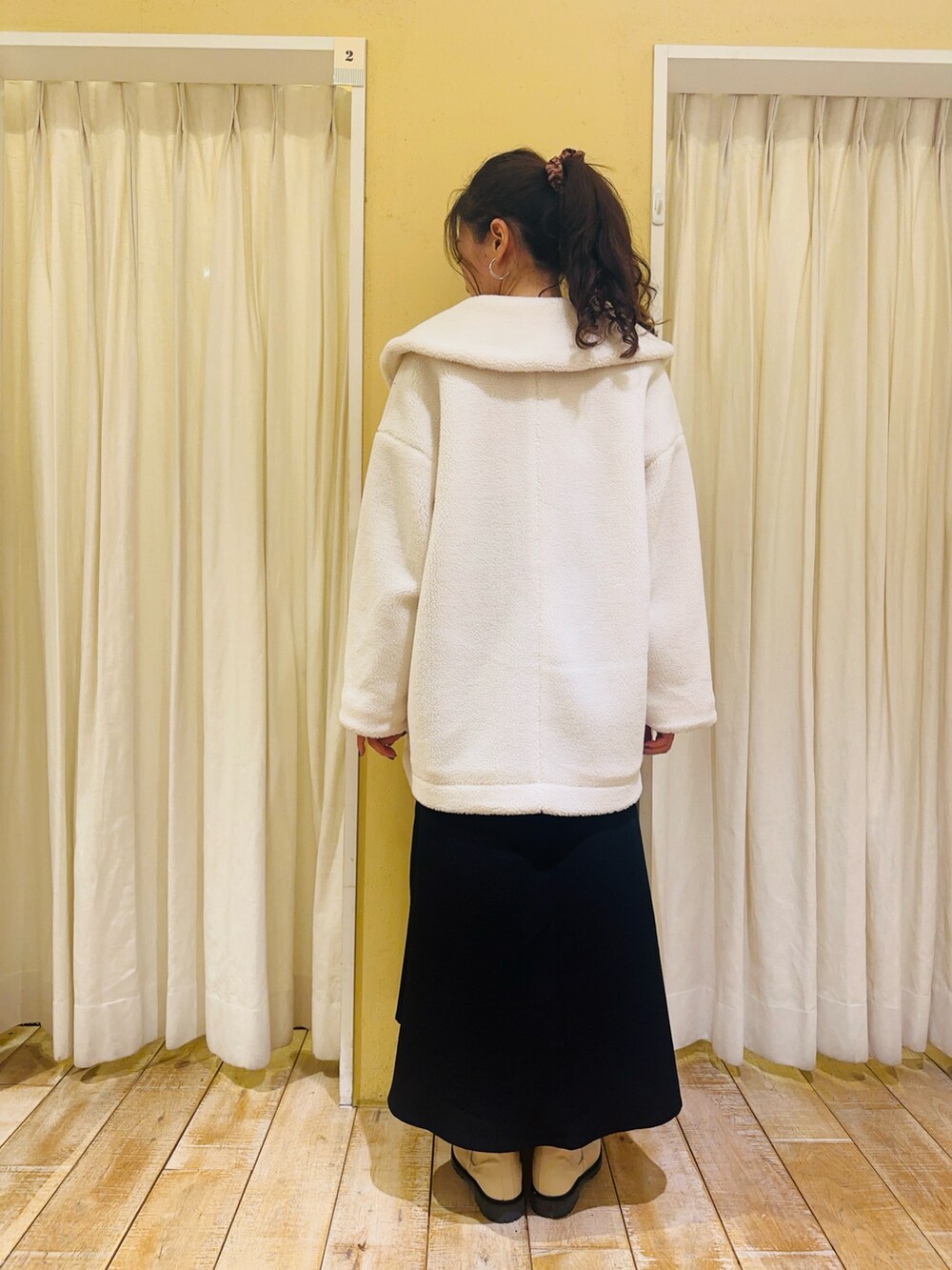 ホワイト系のノーカラージャケット、ベージュ系のニット/セーター、ブラック系のワンピースを着用したレディースの冬コーディネートの2枚目の写真