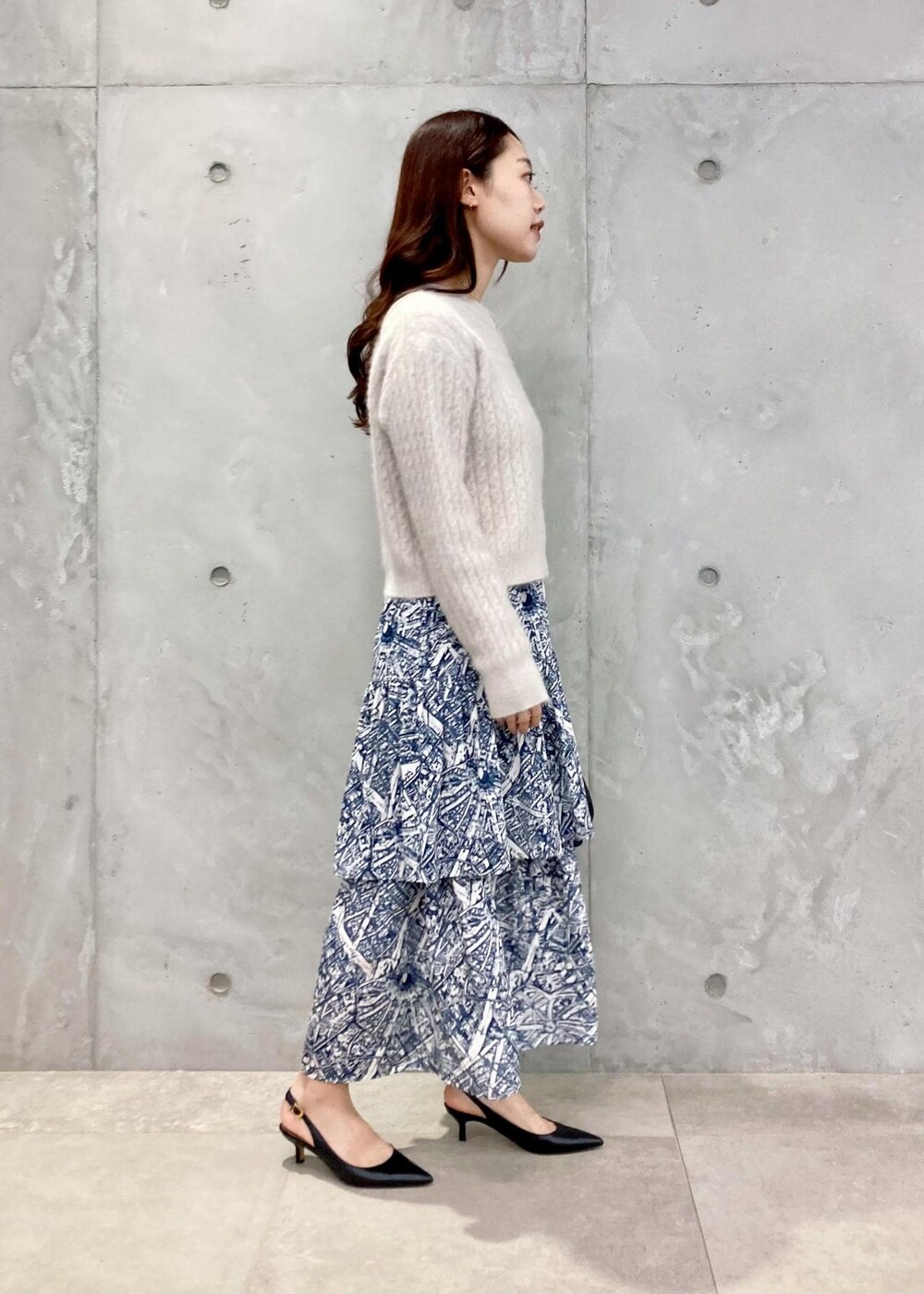 ブラック系のショルダーバッグ、ブラック系のパンプス、ブルー系のスカートを着用したレディースの秋コーディネートの2枚目の写真