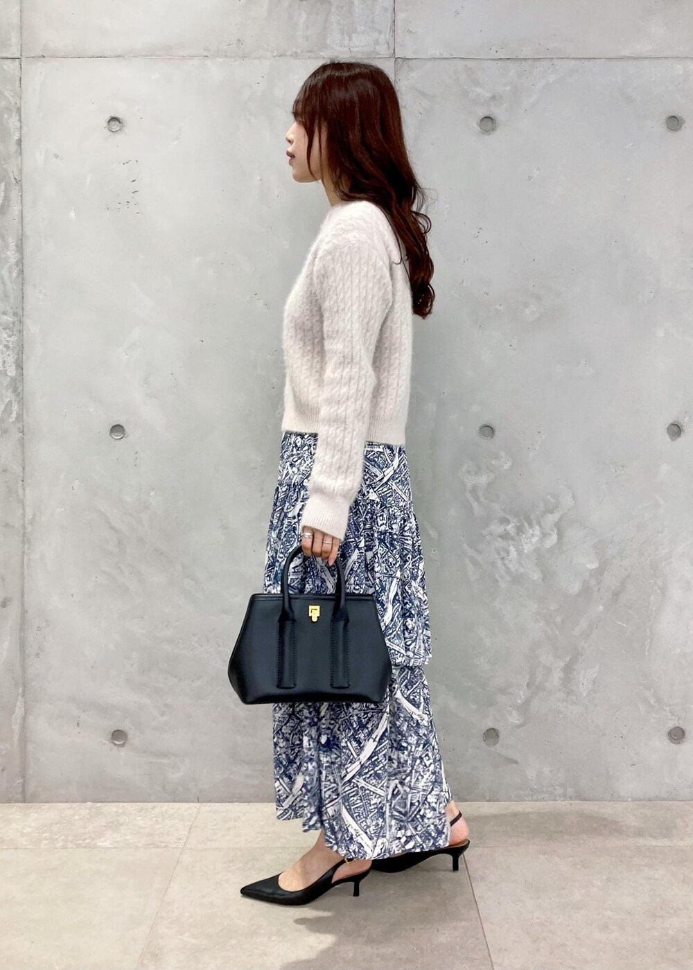 ブラック系のショルダーバッグ、ブラック系のパンプス、ブルー系のスカートを着用したレディースの秋コーディネートの4枚目の写真