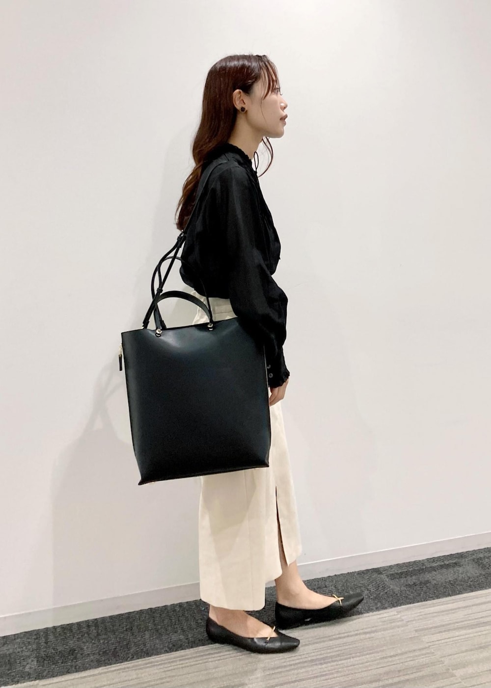 ブラック系のトートバッグ、ブラック系のパンプス、ホワイト系のスカートを着用したレディースの秋コーディネートの2枚目の写真