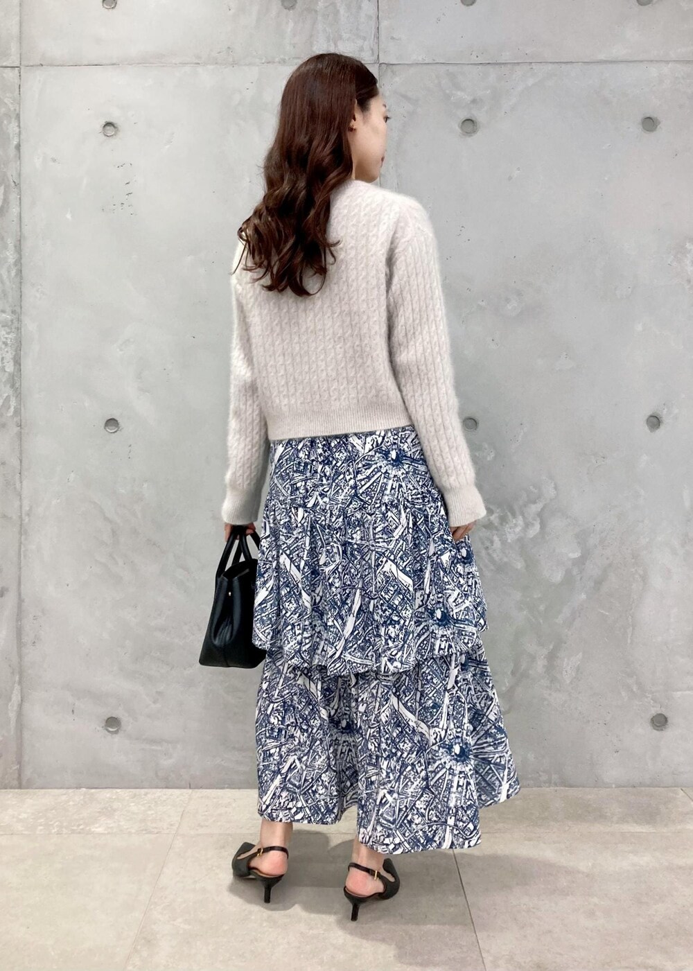 ブラック系のショルダーバッグ、ブラック系のパンプス、ブルー系のスカートを着用したレディースの秋コーディネートの3枚目の写真