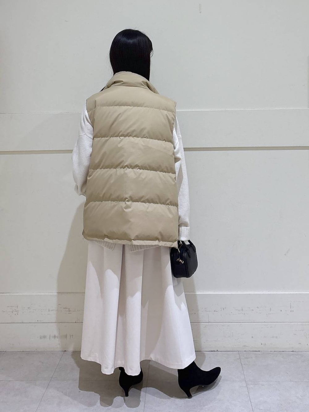 ベージュ系のダウンベスト、ホワイト系のニット/セーター、ブラック系のショルダーバッグを着用したレディースの秋コーディネートの3枚目の写真