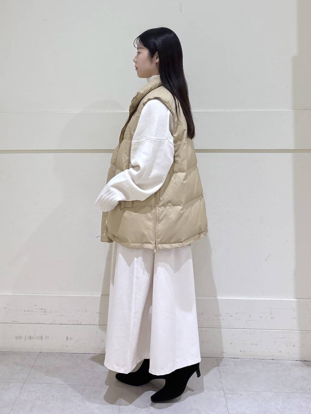 ベージュ系のダウンベスト、ホワイト系のニット/セーター、ブラック系のショルダーバッグを着用したレディースの秋コーディネートの2枚目の写真