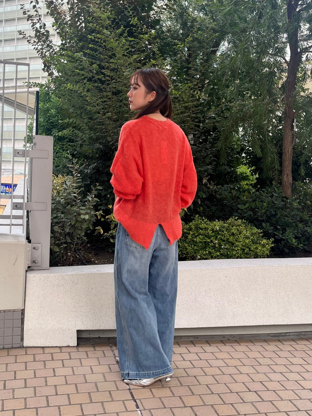 ブルー系のデニムパンツ、ブラウン系のショルダーバッグ、オレンジ系のニット/セーターを着用したレディースの秋コーディネートの2枚目の写真