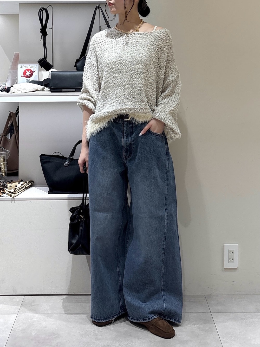 ブルー系のデニムパンツ、ブラック系のトートバッグ、ベージュ系のニット/セーターを着用したレディースの秋コーディネートの2枚目の写真