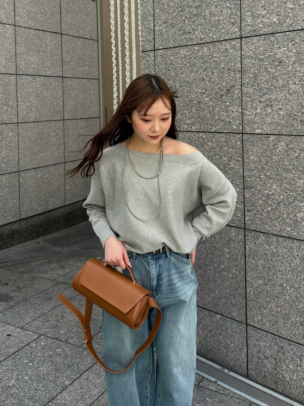 ブルー系のデニムパンツ、グレー系のニット/セーター、ブラウン系のショルダーバッグを着用したレディースの春コーディネートの3枚目の写真