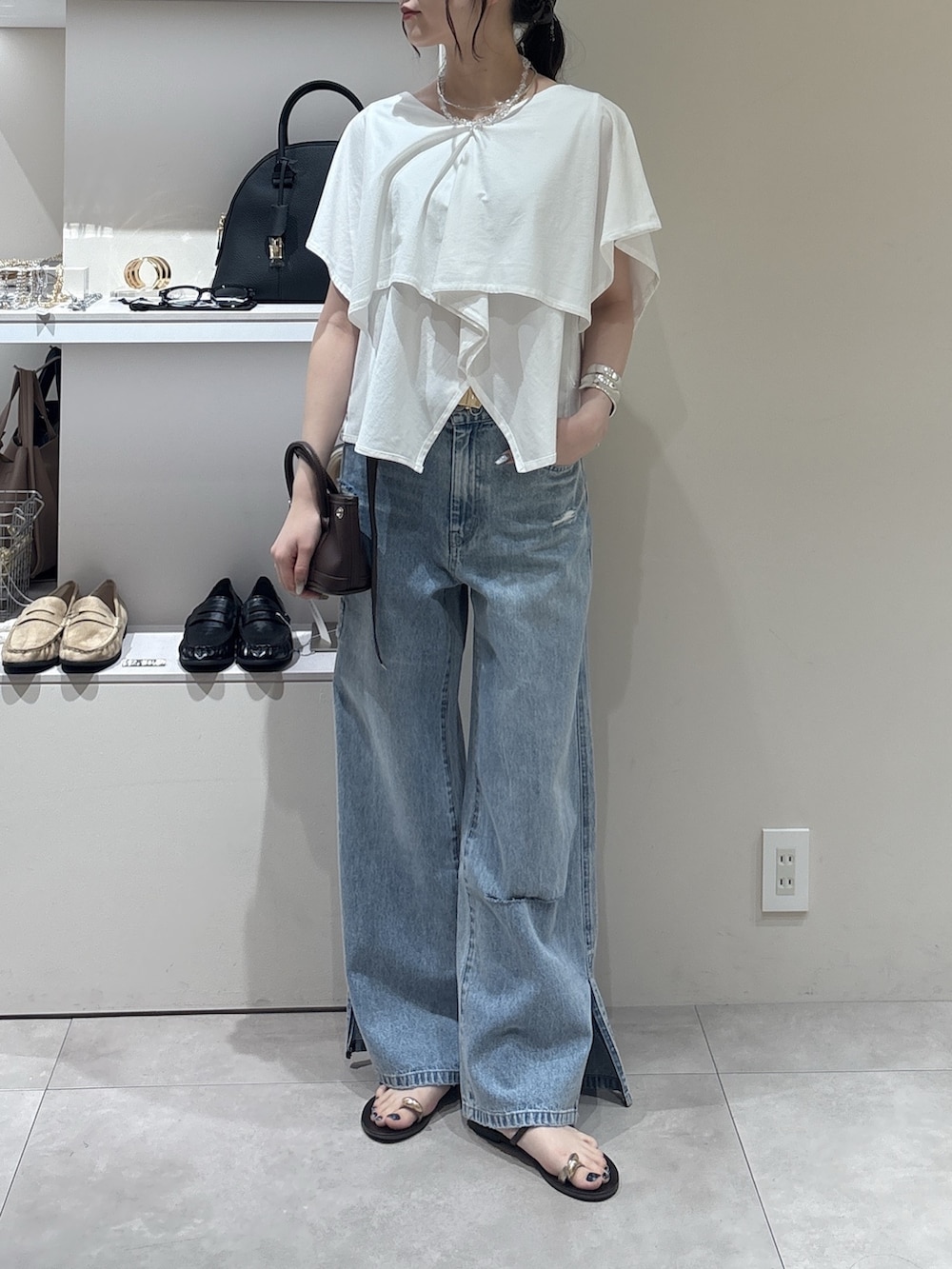 ブルー系のデニムパンツ、ブラウン系のショルダーバッグ、ホワイト系のTシャツ/カットソーを着用したレディースの夏コーディネートの2枚目の写真