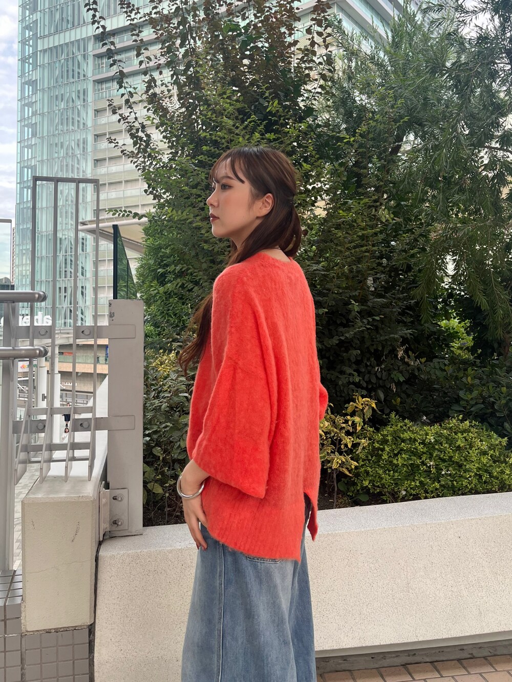 ブルー系のデニムパンツ、ブラウン系のショルダーバッグ、オレンジ系のニット/セーターを着用したレディースの秋コーディネートの4枚目の写真