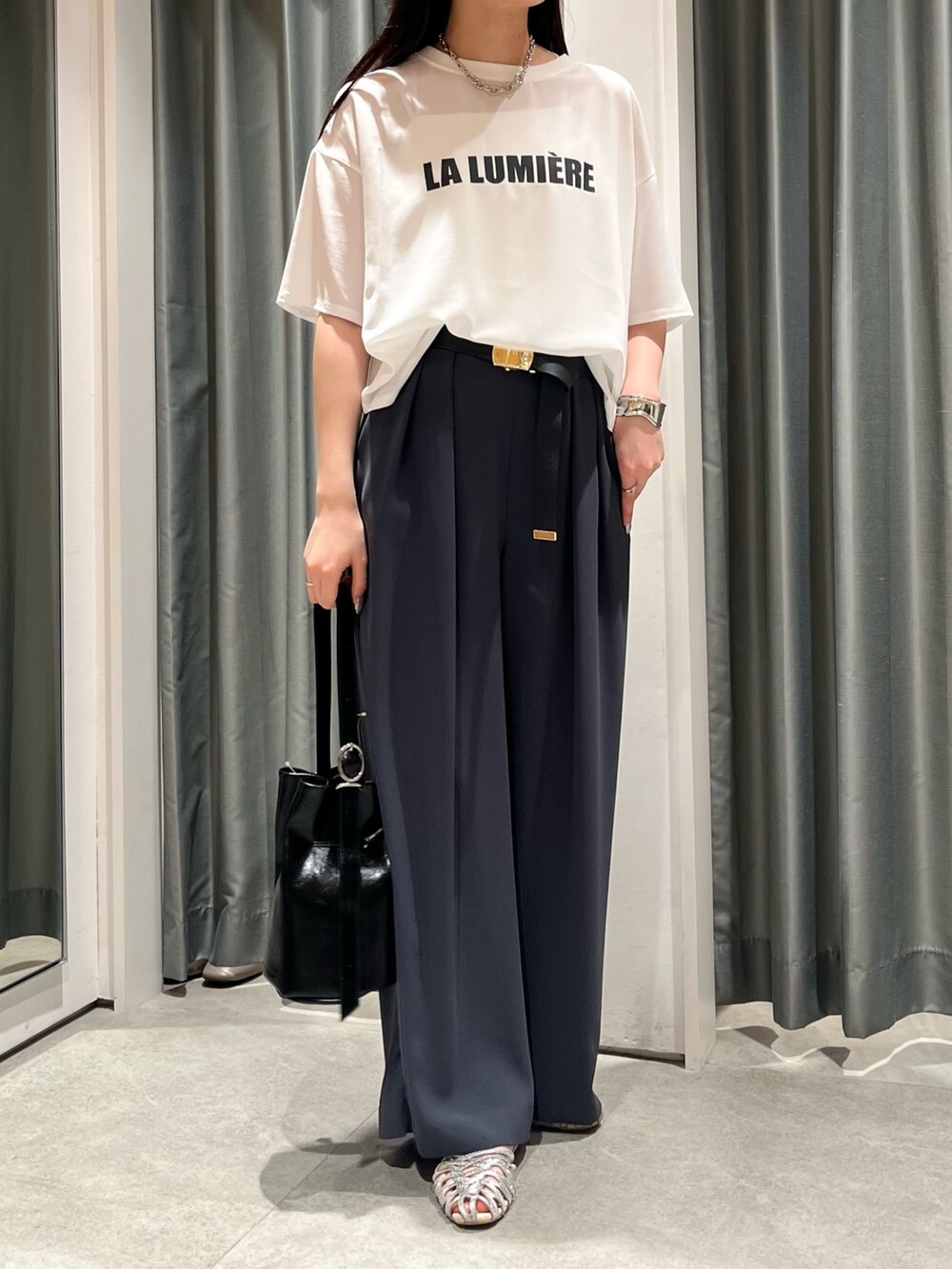 グレー系のスラックス、ブラック系のバッグ、シルバー系のパンプスを着用したレディースの夏コーディネートの2枚目の写真