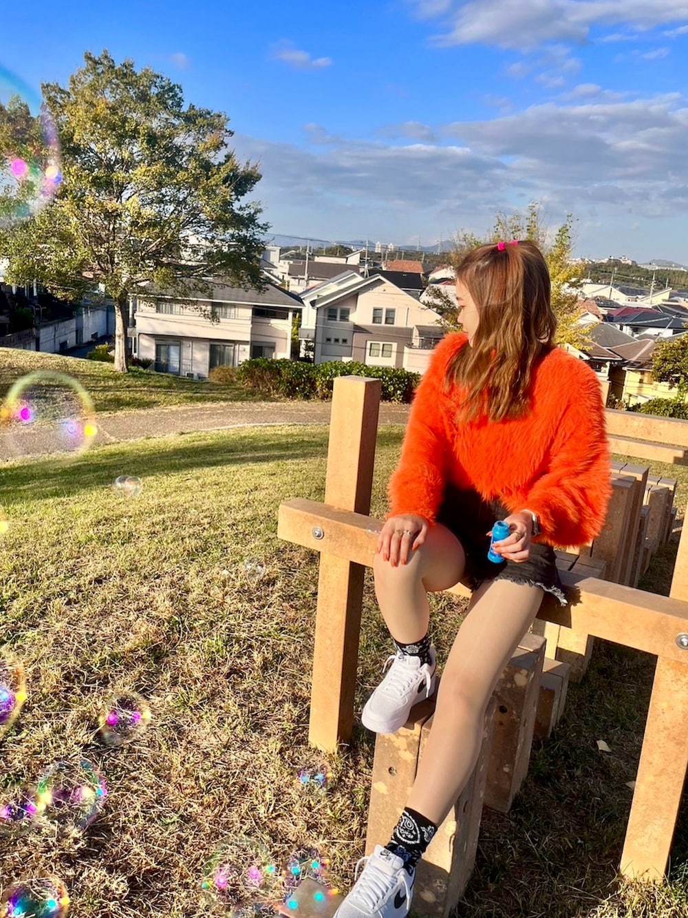 オレンジ系のニット/セーター、ブラック系のパンツ、ホワイト系のスニーカーを着用したレディースの春コーディネートの2枚目の写真