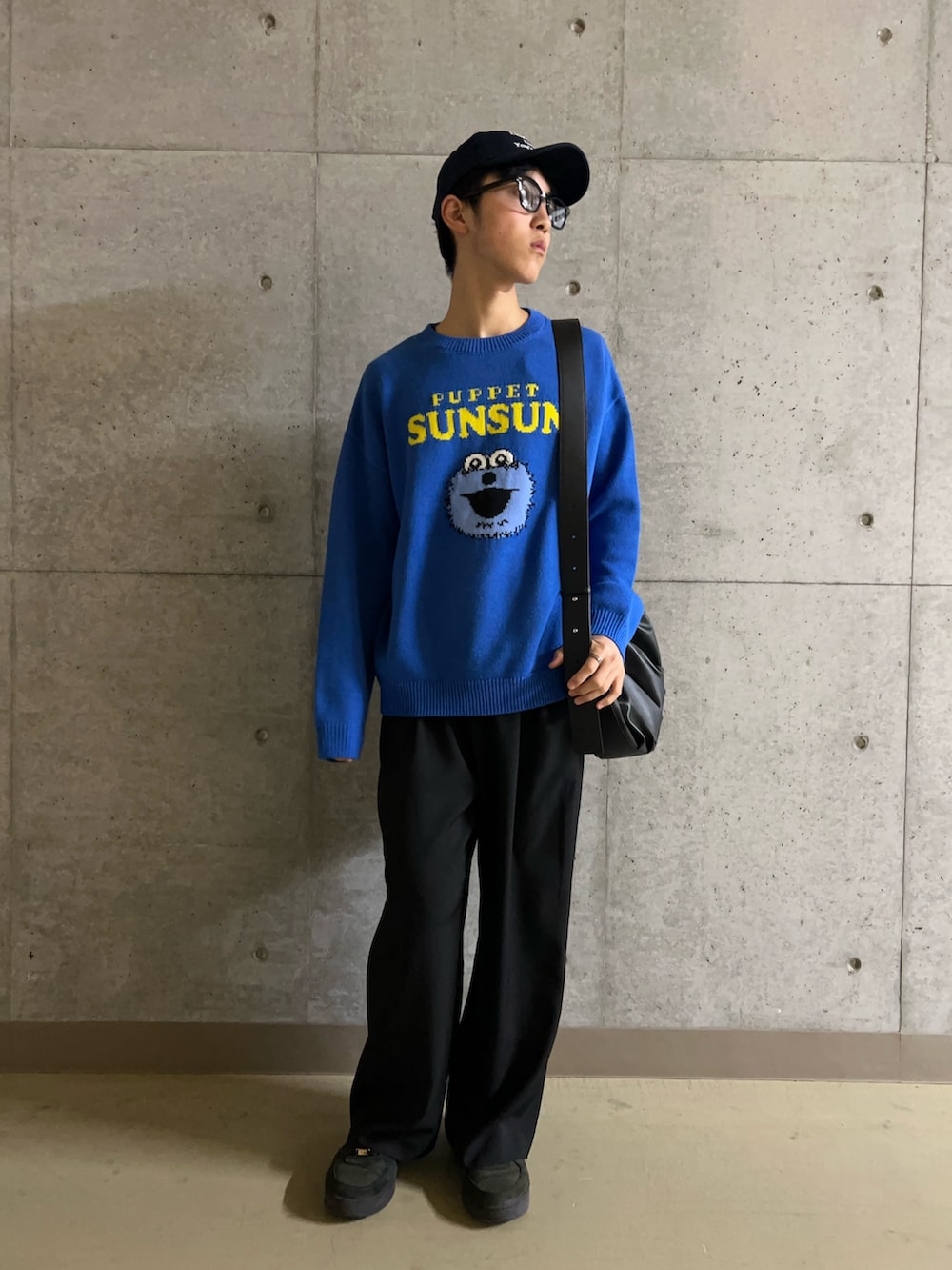 ブラック系のスラックス、ブルー系のニット/セーター、ブラック系のショルダーバッグを着用したメンズの冬コーディネートの2枚目の写真