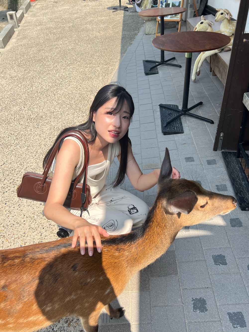 ベージュ系のベスト、ブラウン系のショルダーバッグ、ホワイト系のキャミソールを着用したレディースの夏コーディネートの2枚目の写真