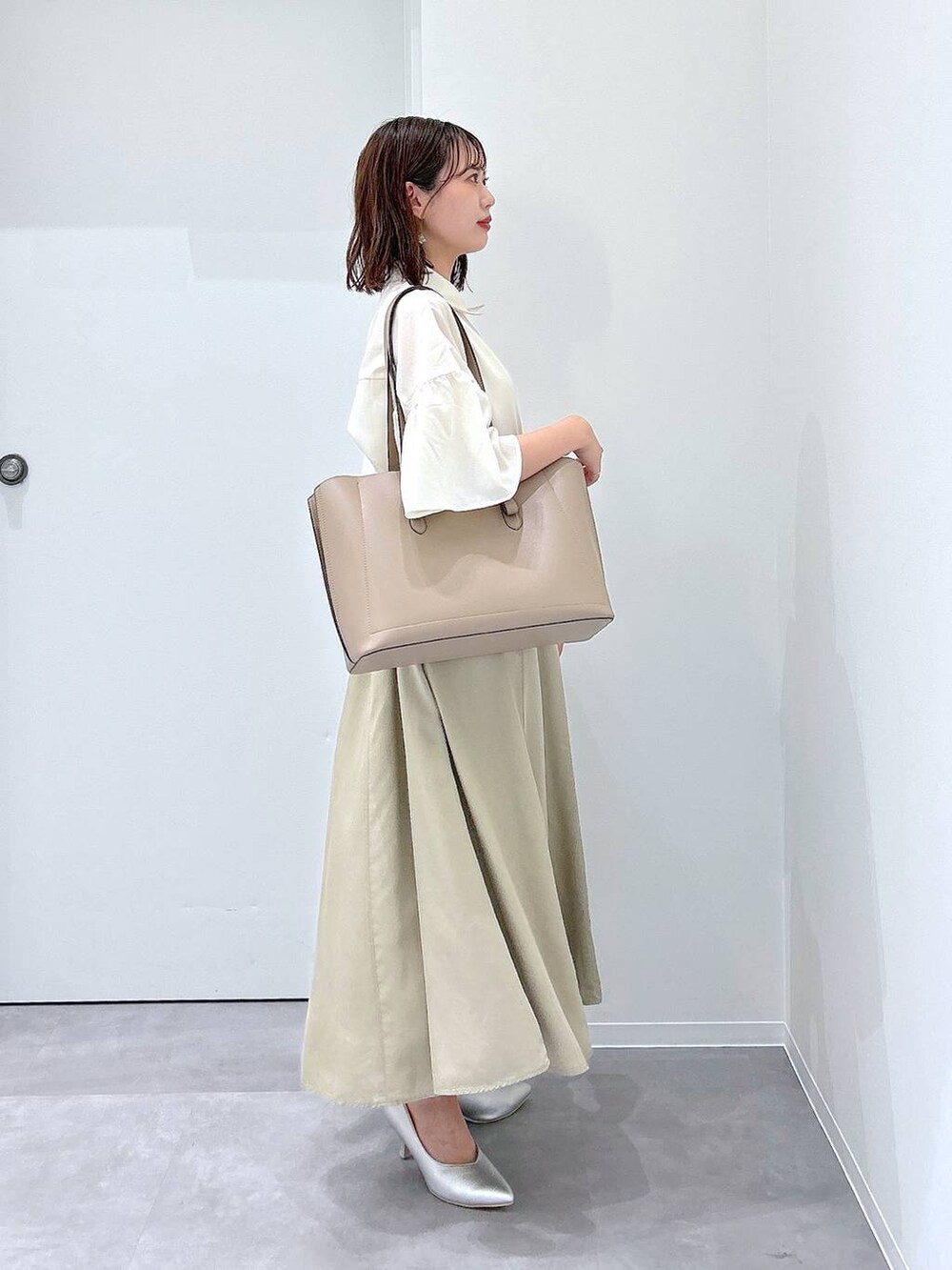 ベージュ系のトートバッグ、シルバー系のパンプス、ベージュ系のスカートを着用したレディースの夏コーディネートの2枚目の写真