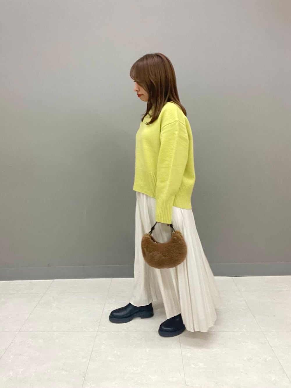 イエロー系のニット/セーター、ブラック系のブーツ、ホワイト系のスカートを着用したレディースの秋コーディネートの3枚目の写真