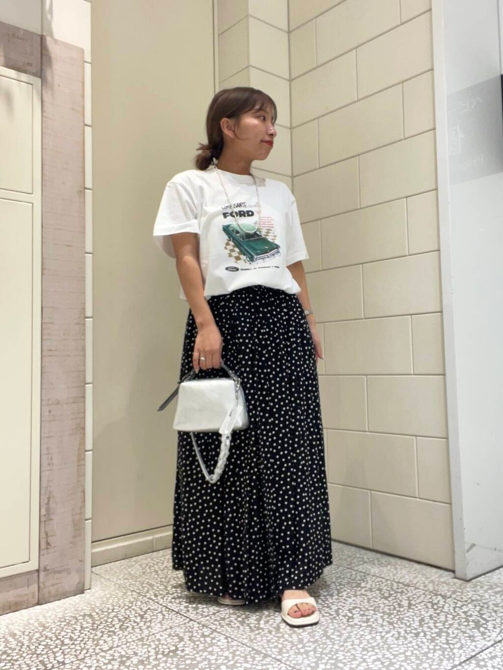 ホワイト系のサンダル、ホワイト系のTシャツ/カットソー、ブラック系のスカートを着用したレディースの夏コーディネートの2枚目の写真