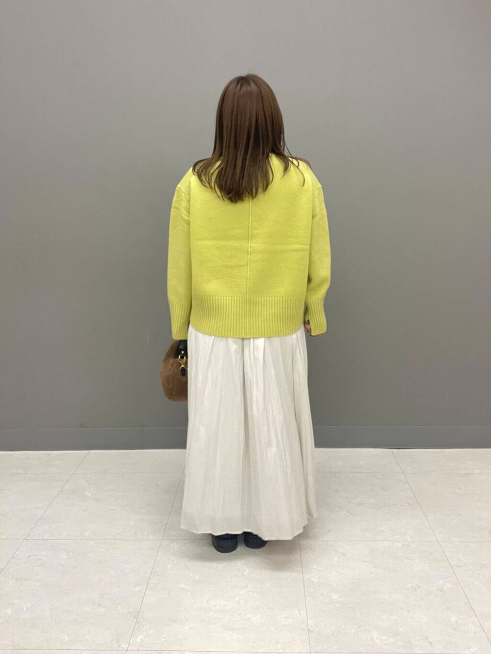 イエロー系のニット/セーター、ブラック系のブーツ、ホワイト系のスカートを着用したレディースの秋コーディネートの4枚目の写真
