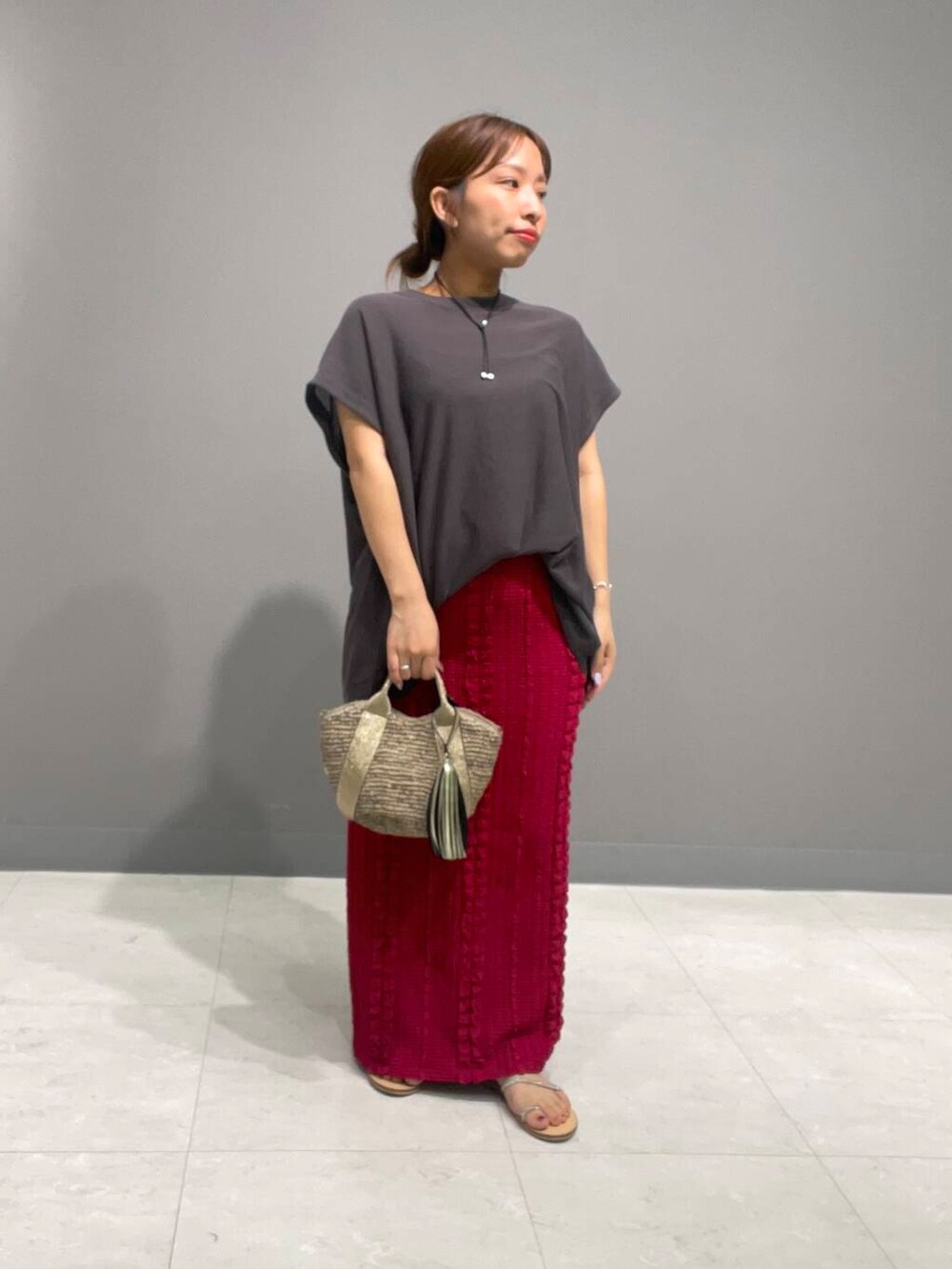 ゴールド系のかごバッグ、グレー系のニット/セーター、レッド系のスカートを着用したレディースの夏コーディネートの2枚目の写真