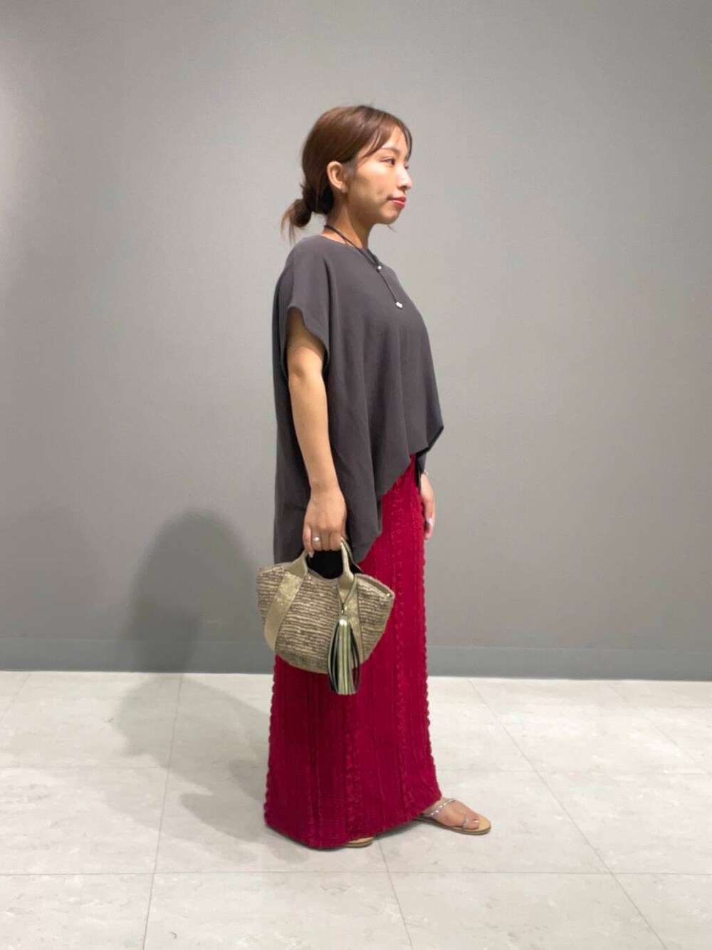 ゴールド系のかごバッグ、グレー系のニット/セーター、レッド系のスカートを着用したレディースの夏コーディネートの3枚目の写真