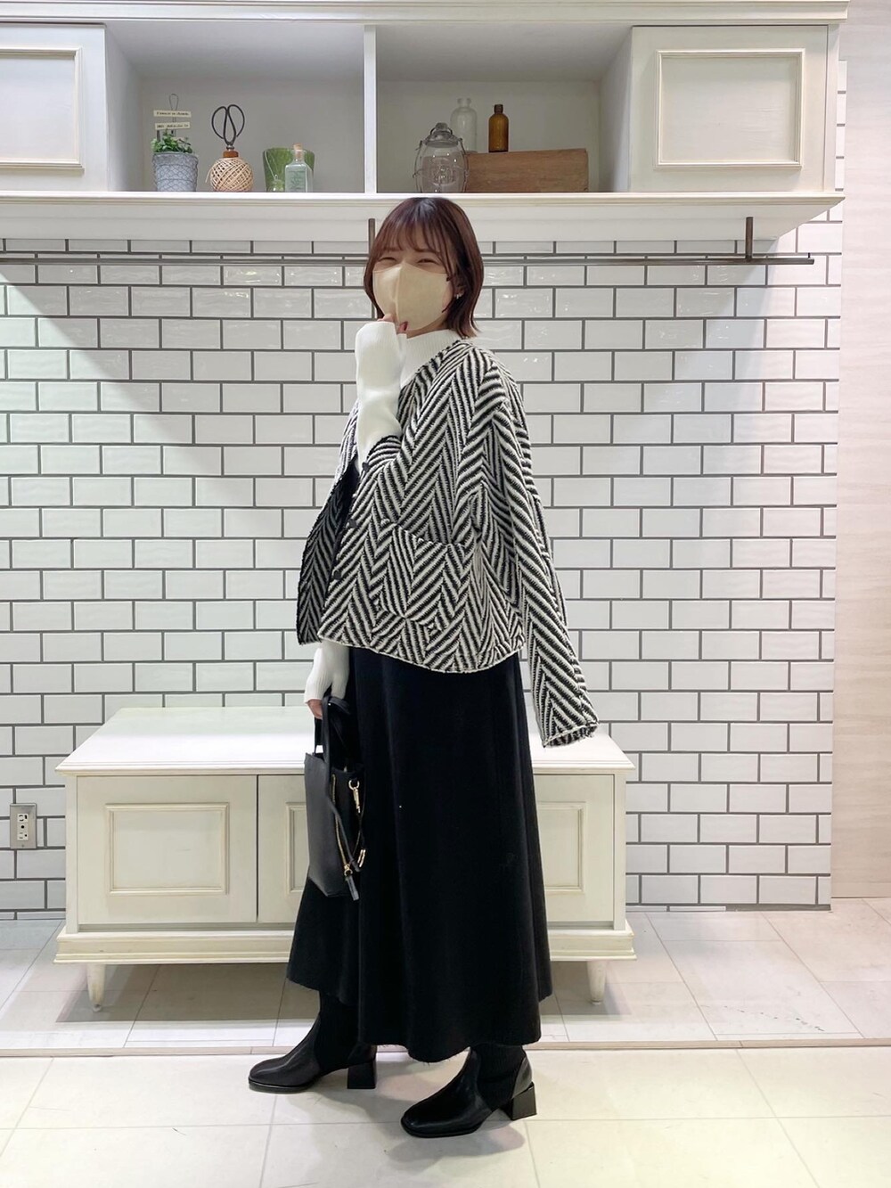 ホワイト系のニット/セーター、グレー系のジャンパースカート、ブラック系のショルダーバッグを着用したレディースの冬コーディネートの2枚目の写真