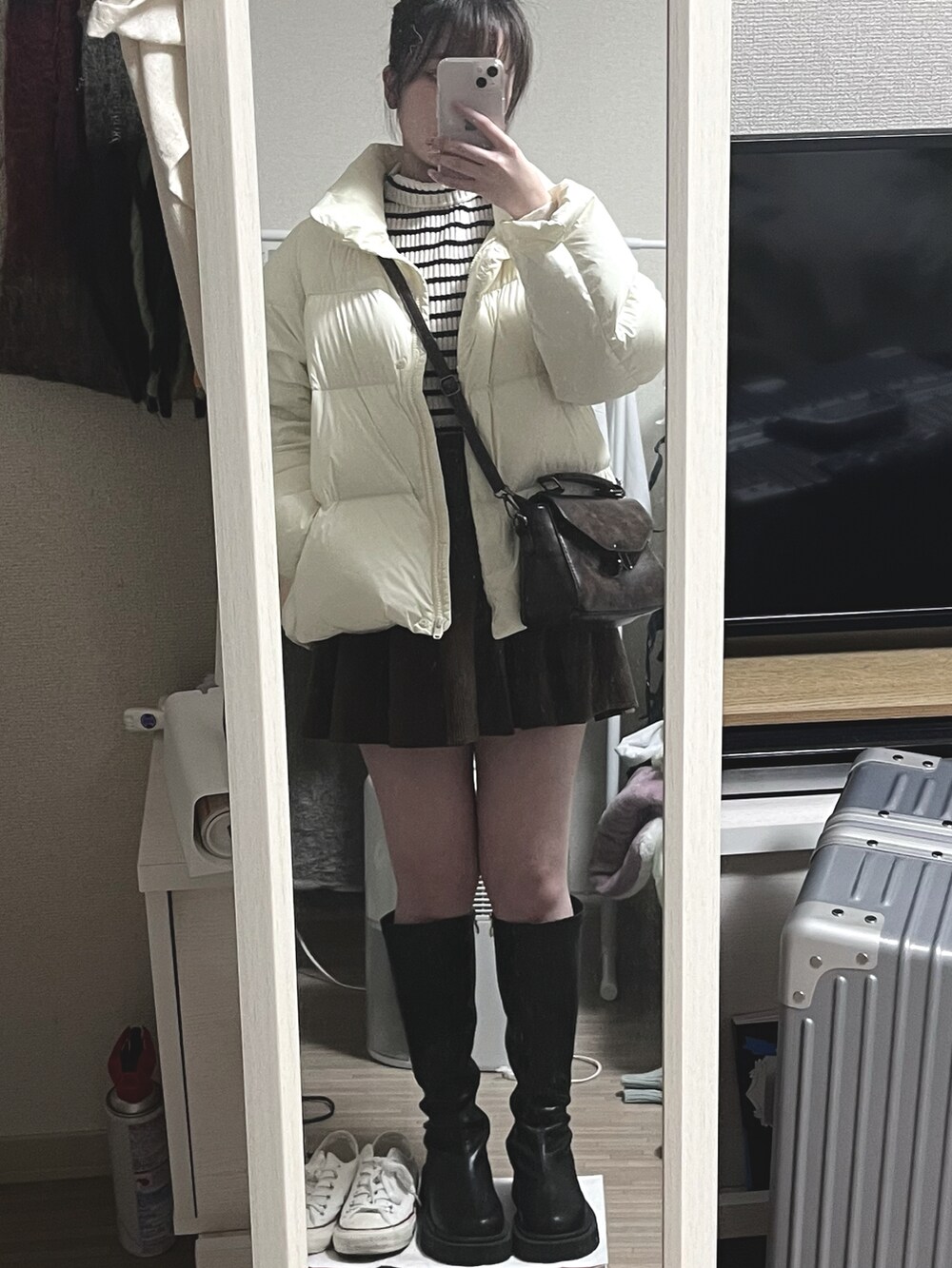 ホワイト系のダウンベスト、ブラウン系のスカート、ブラック系のブーツを着用したレディースの春コーディネートの2枚目の写真