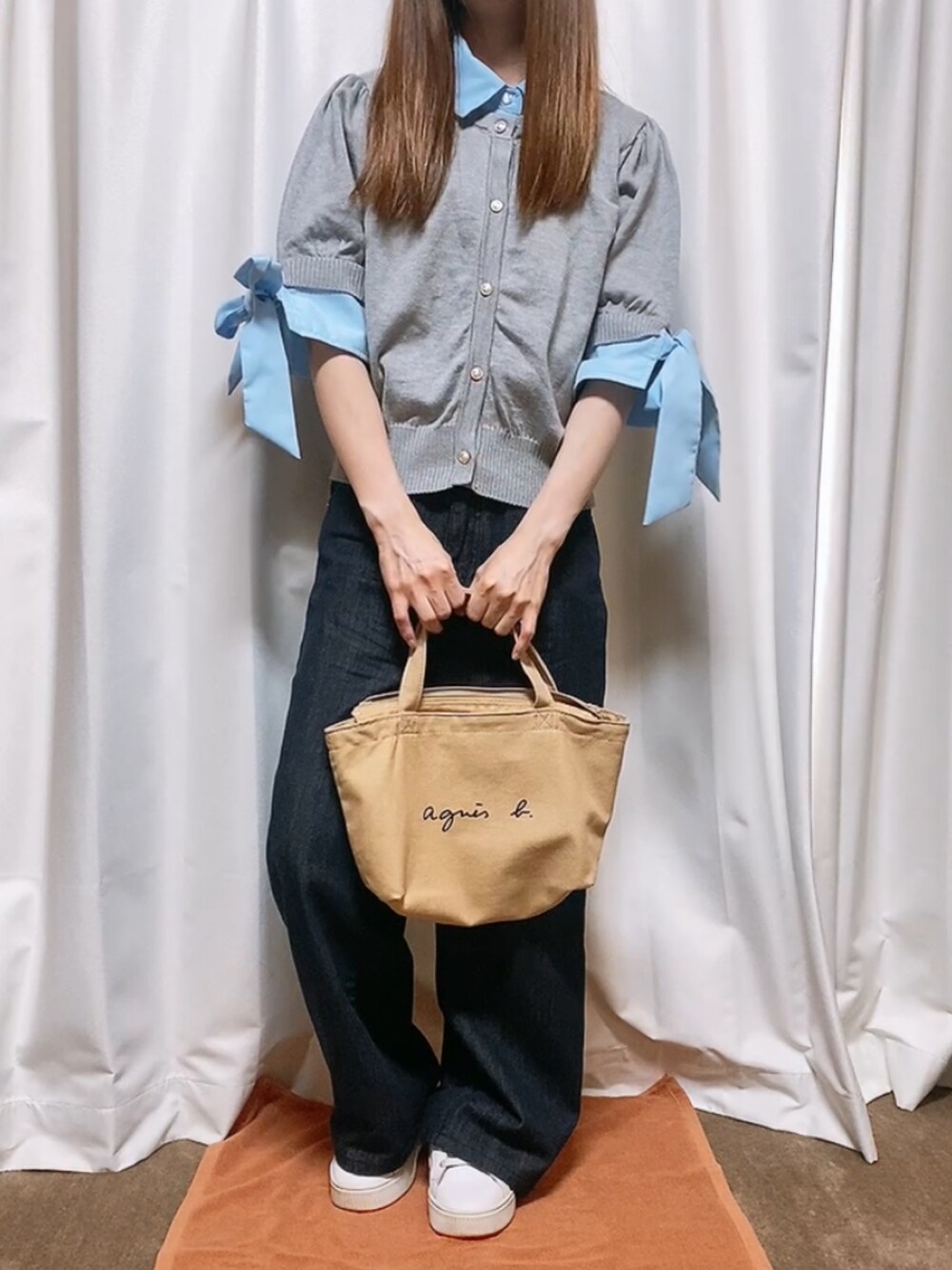 グレー系のトップス、ブルー系のデニムパンツ、ベージュ系のバッグを着用したレディースの秋コーディネートの2枚目の写真