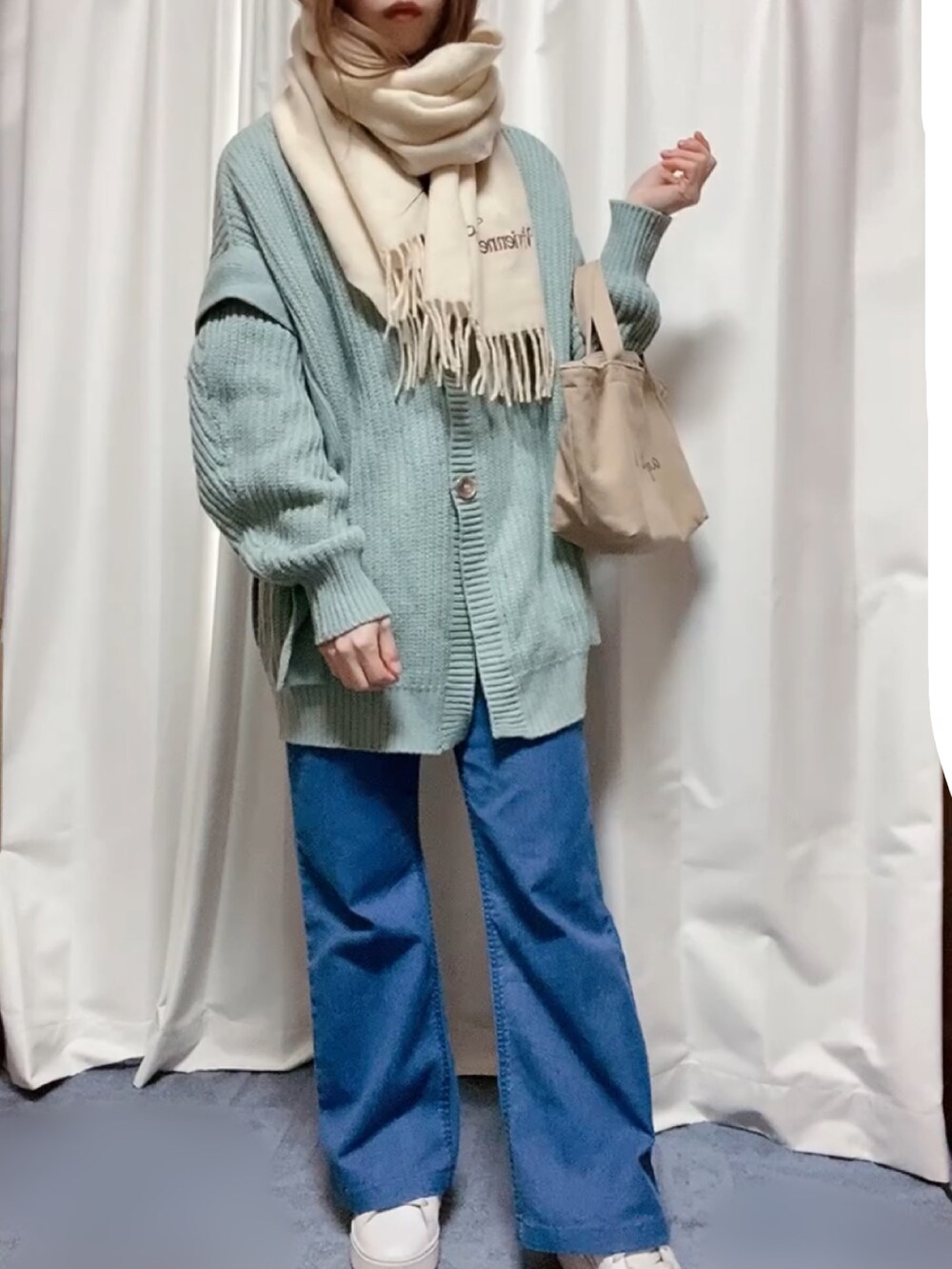ベージュ系のトートバッグ、グリーン系のカーディガン/ボレロ、ブルー系のデニムパンツを着用したレディースの冬コーディネートの2枚目の写真