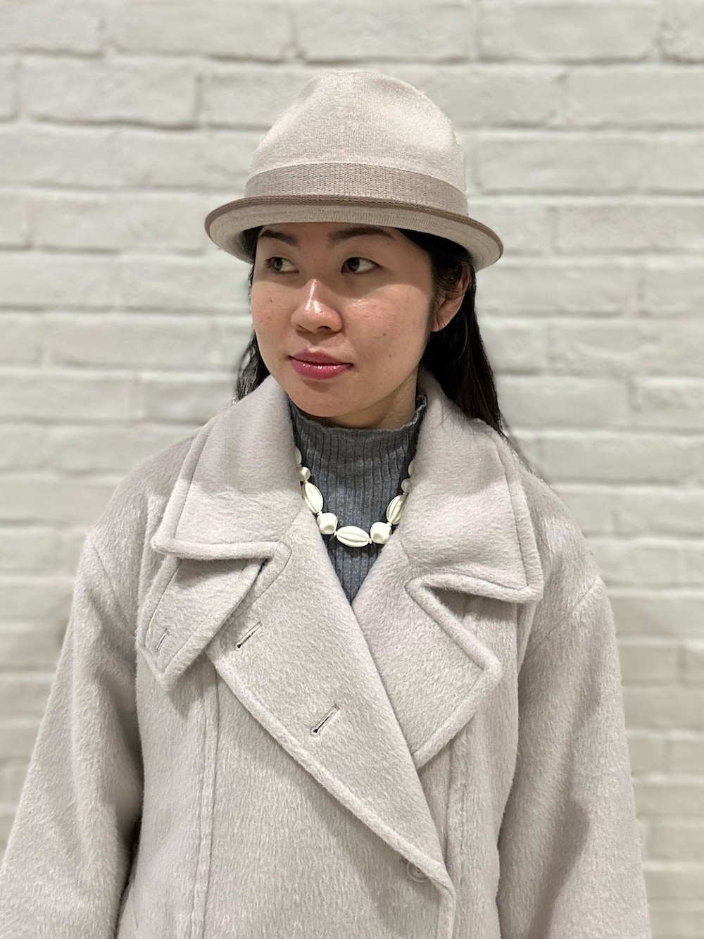 グレー系のニット/セーター、ベージュ系のステンカラーコート、ブラック系のスニーカーを着用したレディースの冬コーディネートの2枚目の写真