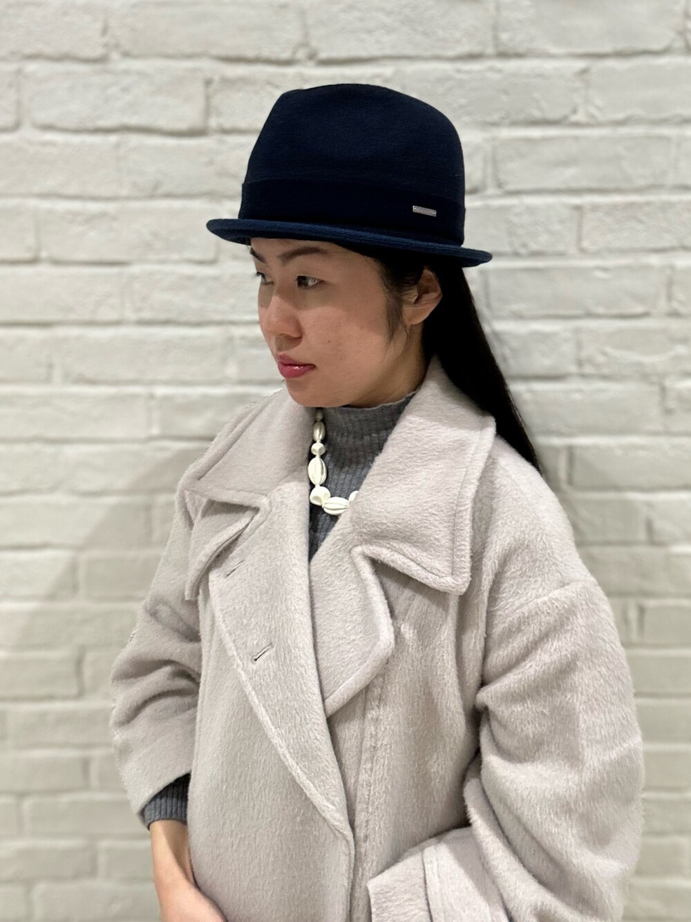 グレー系のニット/セーター、ベージュ系のステンカラーコート、ブラック系のスニーカーを着用したレディースの冬コーディネートの4枚目の写真