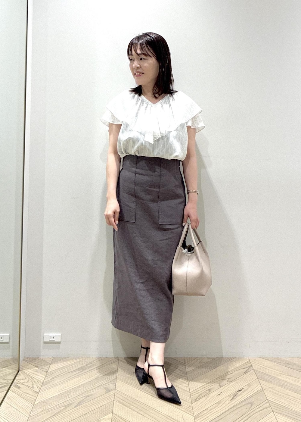 ブラック系のパンプス、グレー系のスカート、ホワイト系のシャツ/ブラウスを着用したレディースの夏コーディネートの3枚目の写真