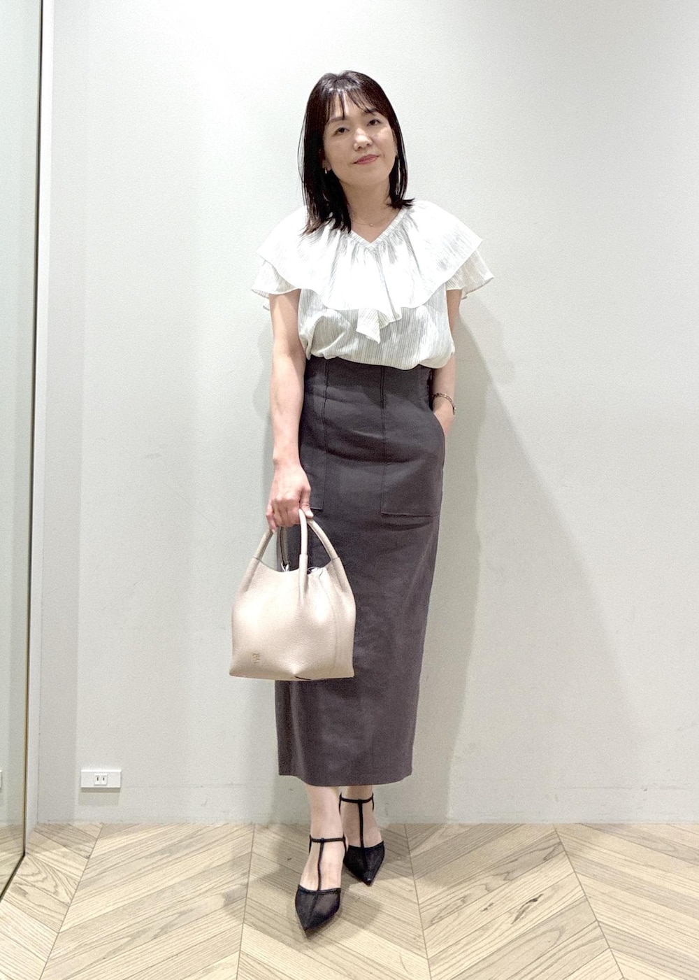 ブラック系のパンプス、グレー系のスカート、ホワイト系のシャツ/ブラウスを着用したレディースの夏コーディネートの2枚目の写真