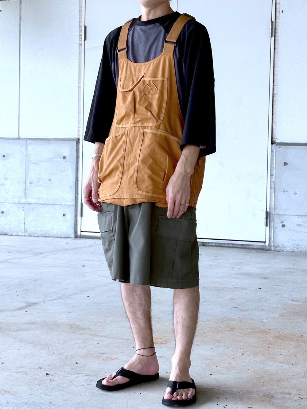 グリーン系のカーゴパンツ、ブラウン系のベスト、ブラック系のTシャツ/カットソーを着用したメンズの夏コーディネートの2枚目の写真