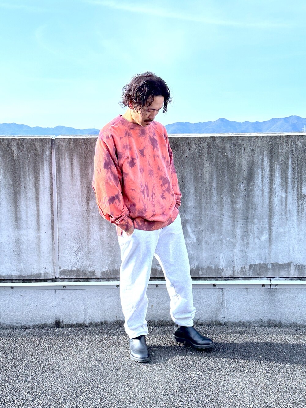 レッド系のスウェット、グレー系のスウェットパンツ、ブラック系のブーツを着用したメンズの春コーディネートの2枚目の写真